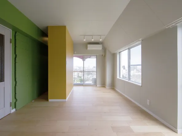 写真：薄い色の床と窓がある白い壁と天井、ドアがある壁は緑に塗られている