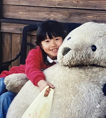 写真：買い物袋を手に持って、自分と同じくらいの大きさのぬいぐるみに抱きついている