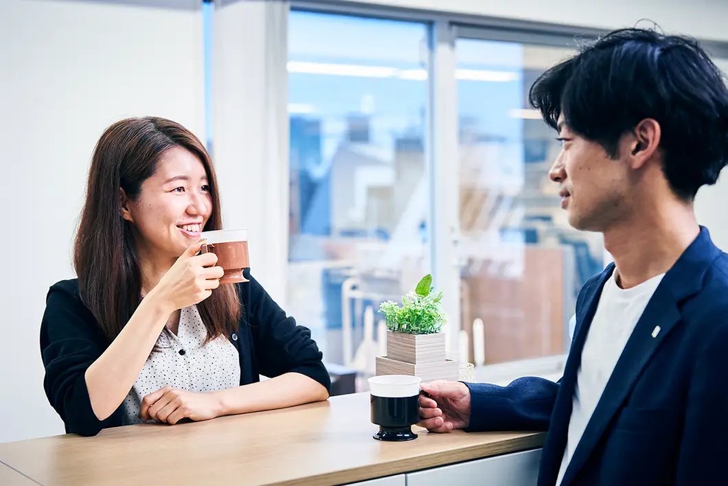 写真：カウンターテーブルで同僚と向かい合わせでコーヒーを飲んでいる